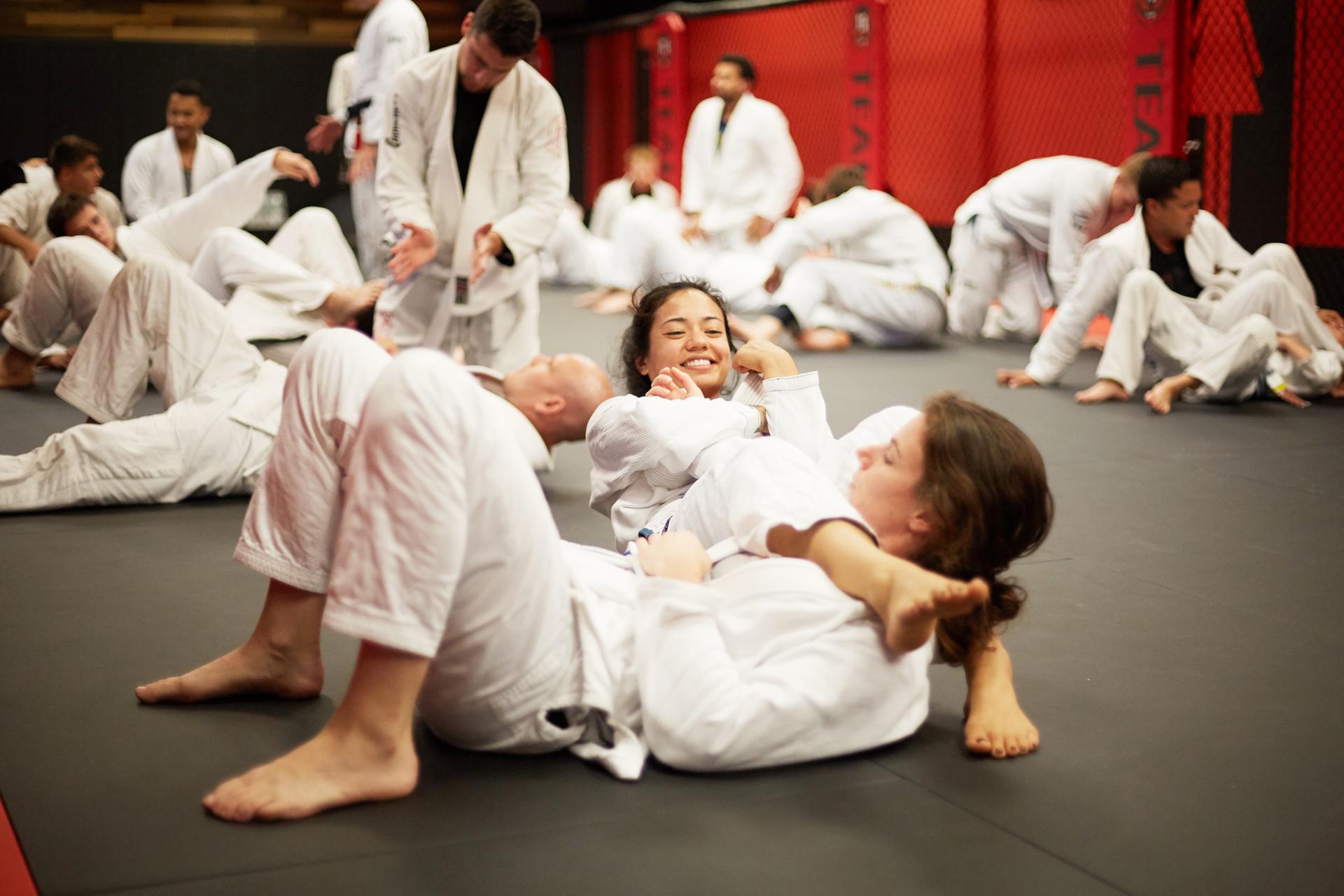 a fun class where two females are practicing jiu jitsu moves with each other and smiling