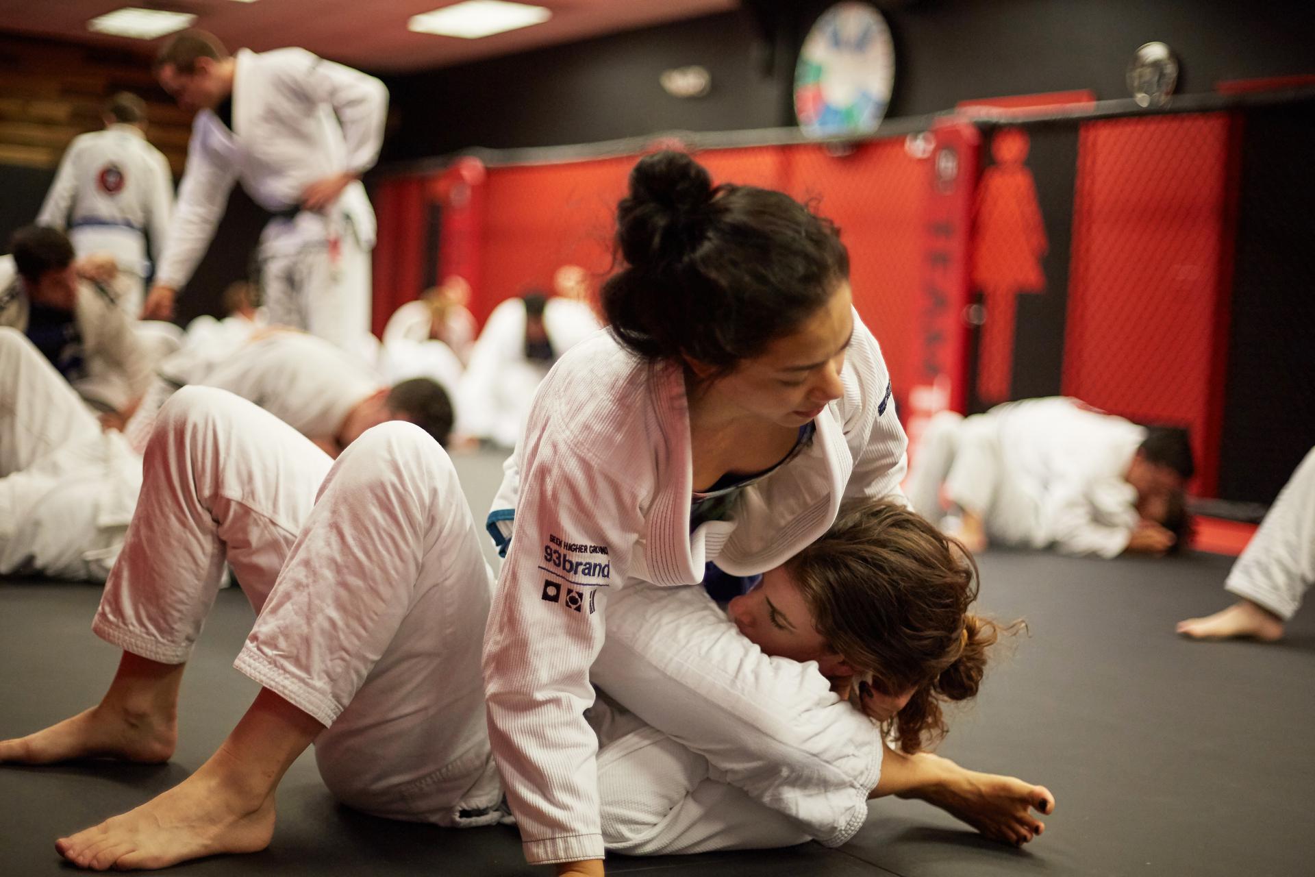 a girls bjj class in full swing as two girl practice a straight armlock