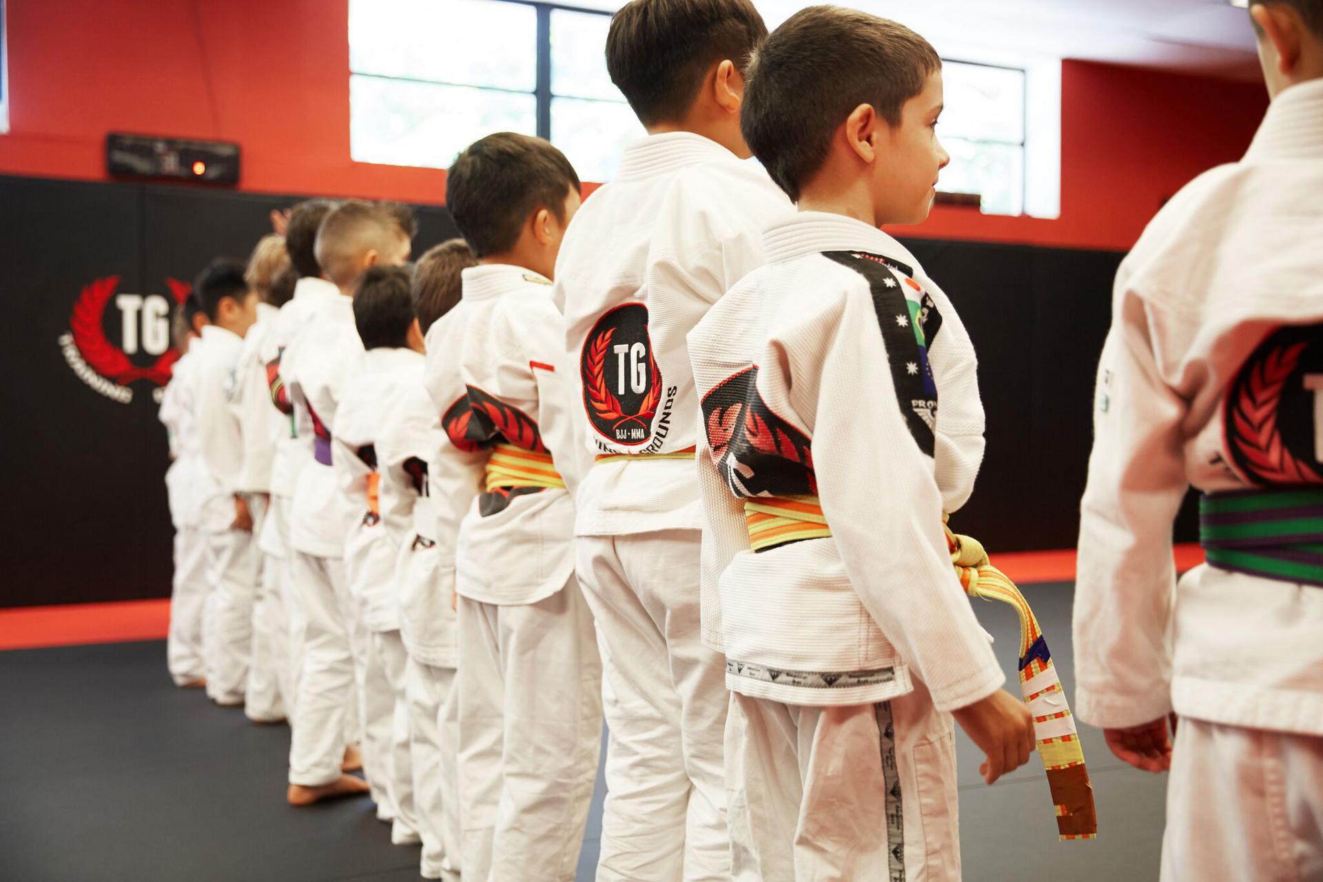 a line of children with their backs turned at the start of a kids martial arts class